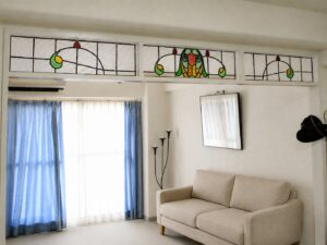 マンションのリビング上部に並ぶ3連の欄間ステンドグラス。泡状の型板ガラスを地に、緑と黄の曲線と赤い雫を組み合わせたアール・ヌーヴォー調の意匠を配している
