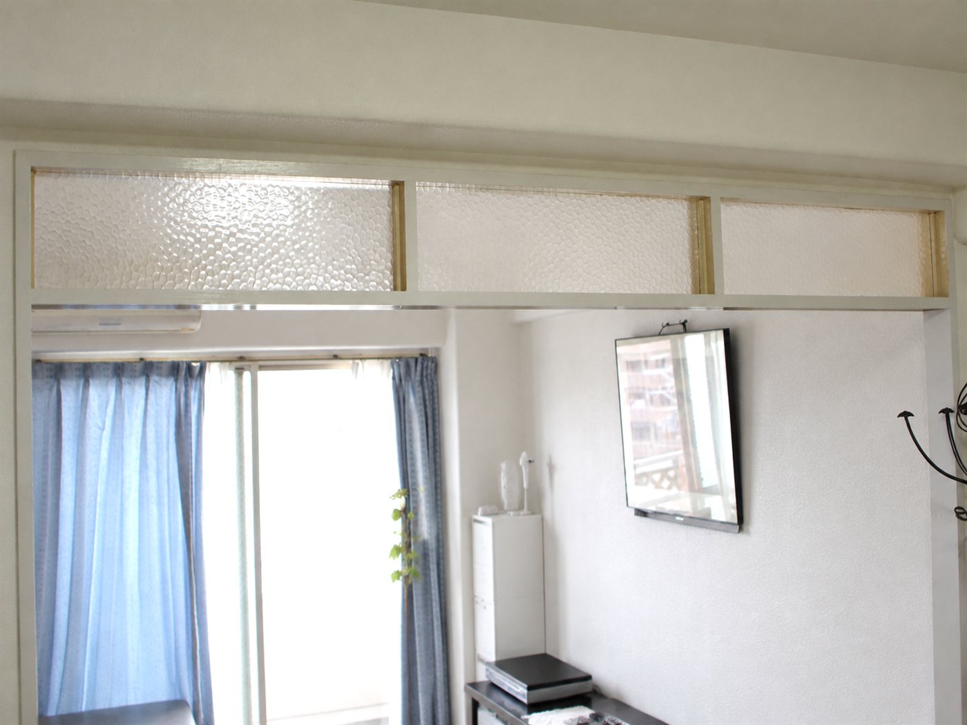施工前のマンションのリビング欄間。3連の開口に、粒状の型板ガラス（すりガラス）が入っている。下には掃き出し窓と青いカーテン